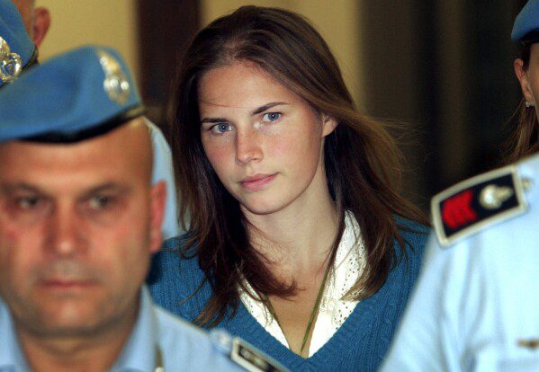 ARCHIVO - El 26 de septiembre de 2008, Amanda Knox, en el centro, es escoltada por agentes de la policía penitenciaria italiana a un tribunal de Perugia.  Amanda Knox se enfrenta a otro juicio por difamación en un caso que podría deshacer el último veredicto de culpabilidad en su contra, ocho años después de que la Corte Suprema de Italia anulara permanentemente su condena por el asesinato de su compañera de cuarto británica de 21 años, Meredith Kercher.  (Foto AP/Pierpaolo Cito, Archivo)